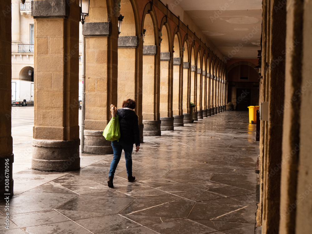 Mujer andado por los arcos de la plaza de la constitución con una bolsa de plástico a su espalda en Donostia