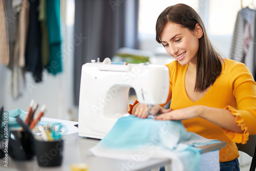 Smiling charming caucasian fashion designer sitting in her studio and sewing beautiful evening dress. photo