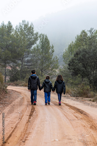 Three children holding hands on a foggy road © Victor