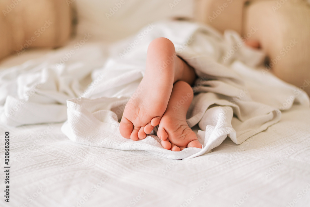 Feet of little sleeping child under white blanket on the bed. Feet of little sleeping child under white blanket on the bed.