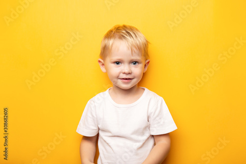 2 years portrait of little blond happy caucasian blue eyes baby boy wearing on white t shirt on yellow background with copy space