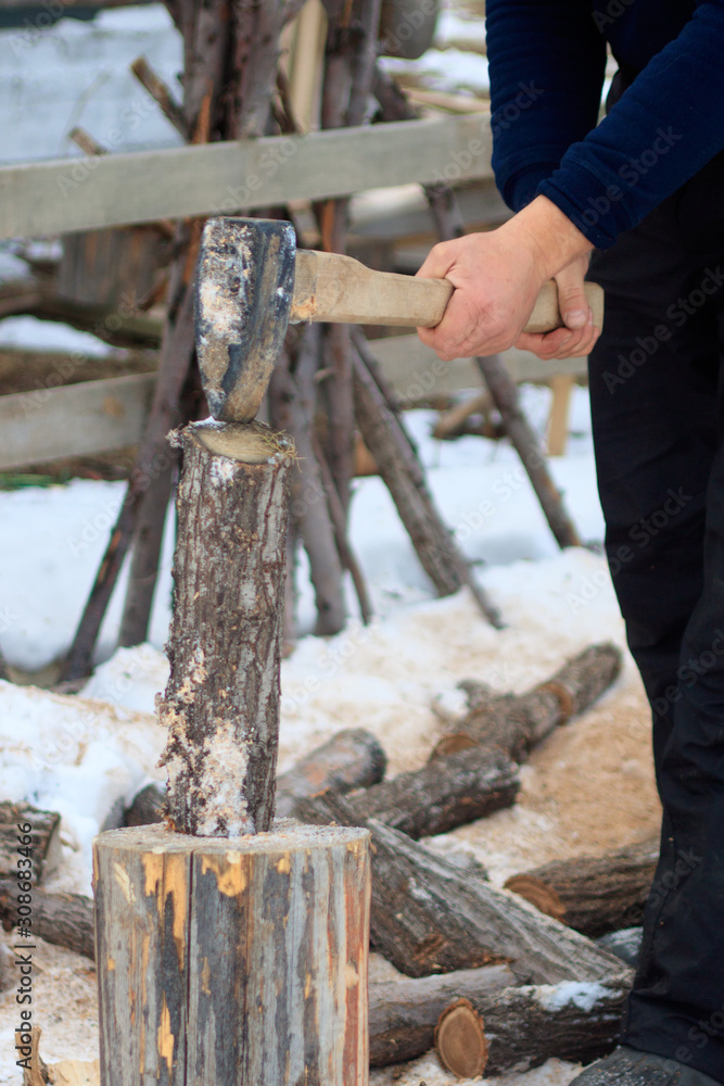 Adult smiling man chopping wood with an ax near his wooden house in the village Adult smiling man chopping wood with an ax near his wooden house in the village