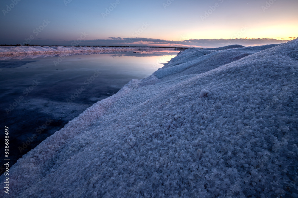 Obraz premium Nature reserve Saline Margherita di Savoia, Apulia, Italy: The salt pan. Salt flats area for sea salt production. A salt marsh, an ecosystem on Adriatic sea. Heaps of salt at sunset ready for harvest