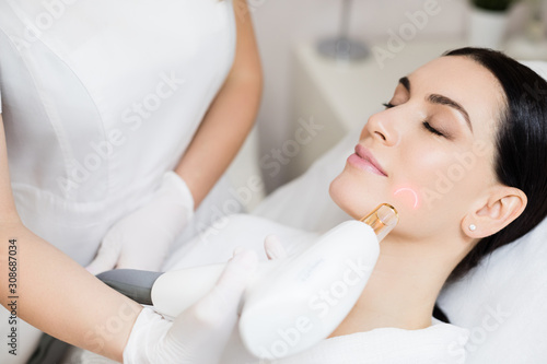 Hardware cosmetology. Face skin care. Skin remodeling. Smiling woman getting facial laser treatment. Dermatologist using laser for skincare treatment of a client removing scars.