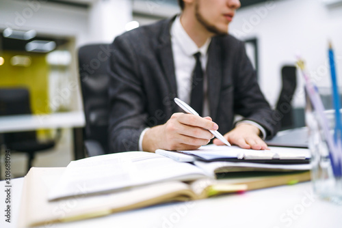 Pen in office worker hand. Close up of the hands of a businessman in a suit signing or writing a document on a sheet of white paper using a pen. Working online concept, business concept.