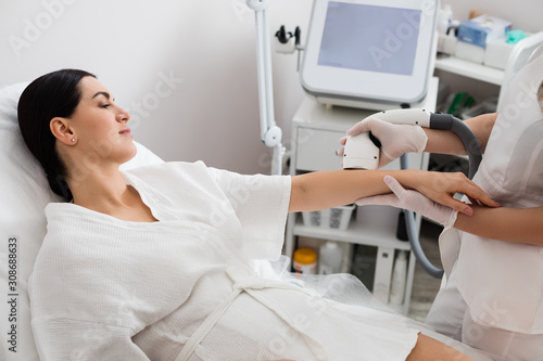 Hardware cosmetology procedure from a therapist. Attractive woman is receiving the laser epilation of her hands in beauty salon.