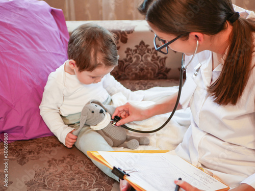 Childrens doctor listens to a child with a phonendoscope. the doctor is at home. call the address. Doctor on call. Phonendoscope, stethoscope. The doctor listens to the breath of a child with a phonen photo