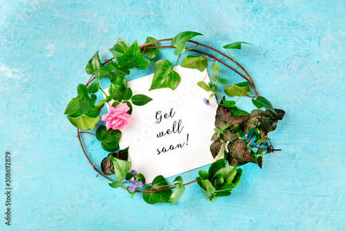 Get well soon card with a wreath of green ivy leaves and a tender pink rose, overhead shot on a blue background photo