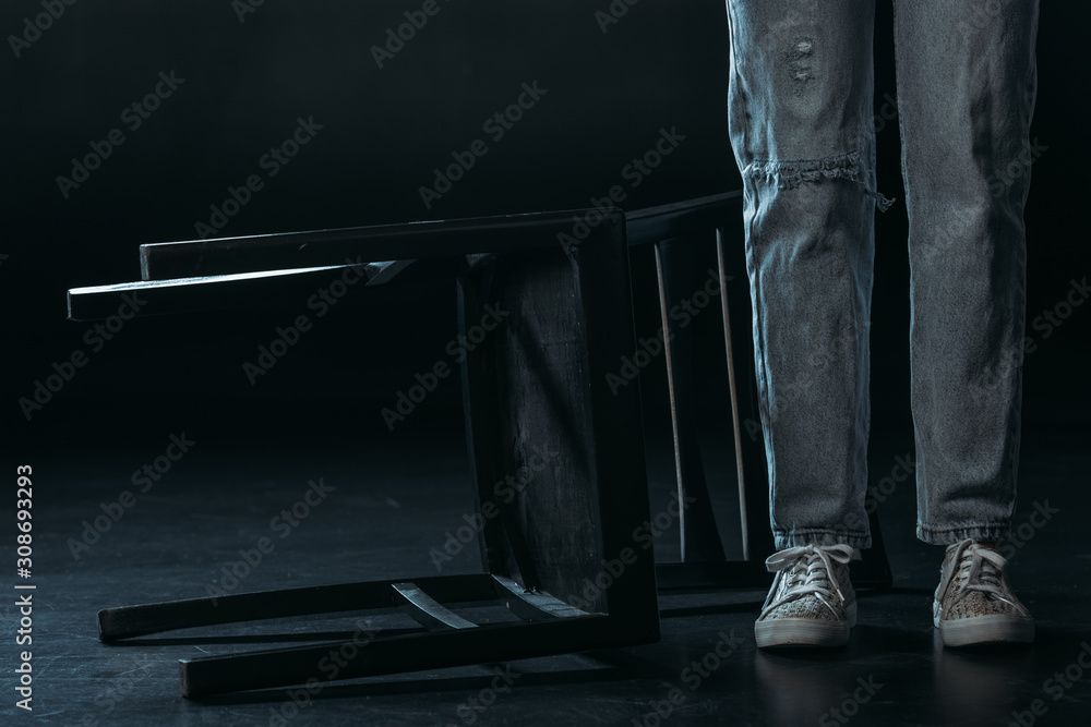 Fototapeta przycięty widok kobiety stojącej w pobliżu upadłego krzesła na czarnym tle