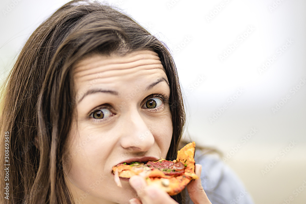 Attractive brunette woman wants to eat pizza slice, looking at it, on light background. Close up. Copy space.