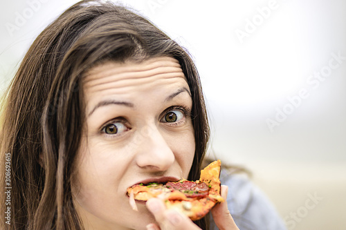 Attractive brunette woman wants to eat pizza slice  looking at it  on light background. Close up. Copy space.