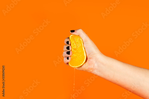 Mano sosteniendo y exprimiendo media naranja sobre fondo naranja. Vista de frente. Copy space