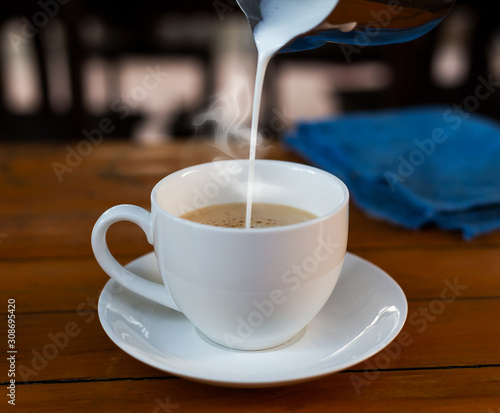 Pour the milk into the coffee in a white cup