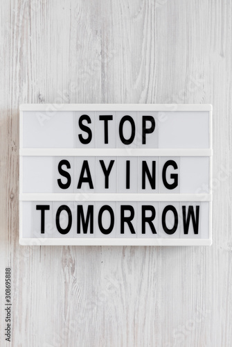 'Stop saying tomorrow' words on a modern board on a white wooden background, top view. Overhead, from above, flat lay.