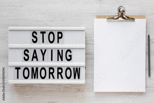 Fototapeta Naklejka Na Ścianę i Meble -  'Stop saying tomorrow' words on a lightbox, clipboard with blank sheet of paper on a white wooden background, top view. Overhead, from above, flat lay.