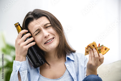 Brunette woman is sad, because of eating and drinking unheathy products. She is stressed with hand with beer on head. Close up. photo