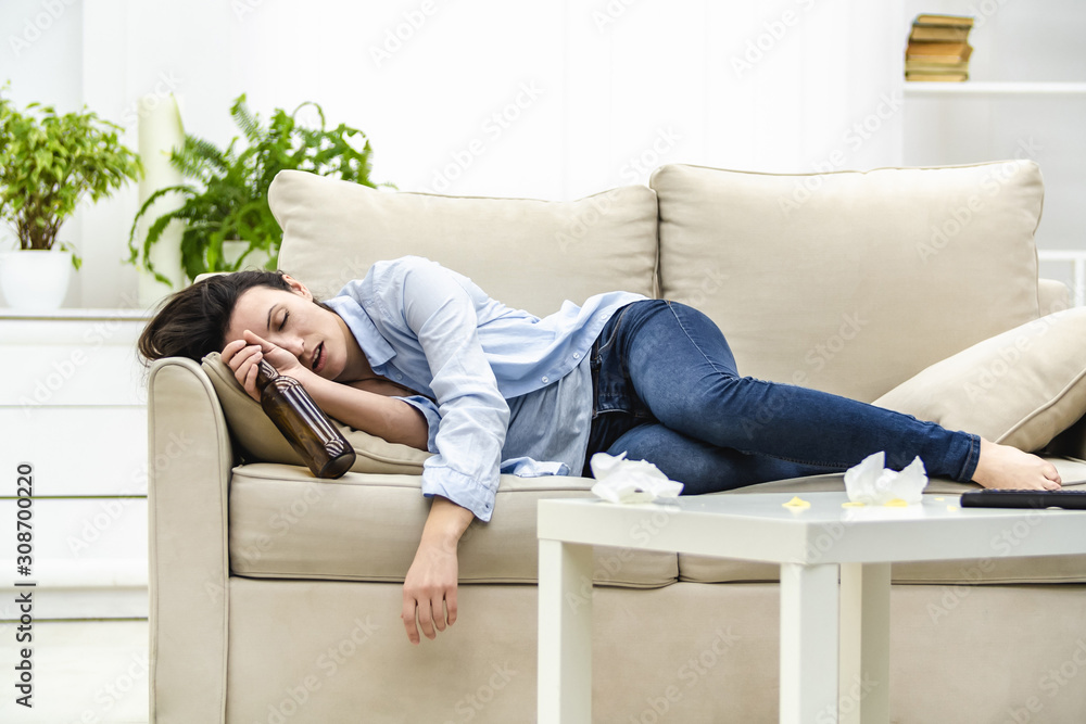 Unconscious drunk woman with empty bottle in her hand is sleeping on the sofa. Unconscious drunk woman with empty bottle in her hand is sleeping on the sofa.