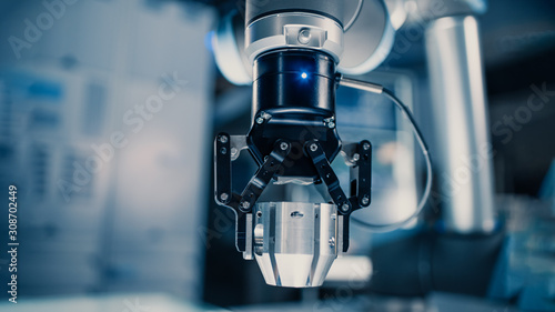 Close Up of a Futuristic Robotic Arm Moving a Metal Object and Placing It. Team of Engineers Observe This Advanced Process. They are in a High Tech Research Laboratory with Modern Equipment.