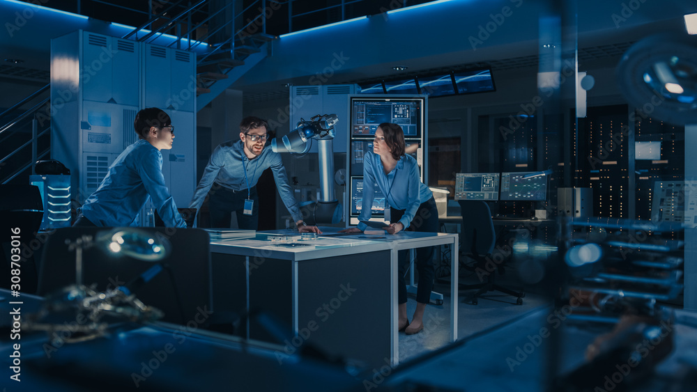 Futuristic Metal Robotic Arm is Moving a Metal Object. Senior Engineer Talks Through This Advanced Process with His Diverse Team. They are in a High Tech Research Laboratory with Modern Equipment. Futuristic Metal Robotic Arm is Moving a Metal Object. Senior Engineer Talks Through This Advanced Process with His Diverse Team. They are in a High Tech Research Laboratory with Modern Equipment.