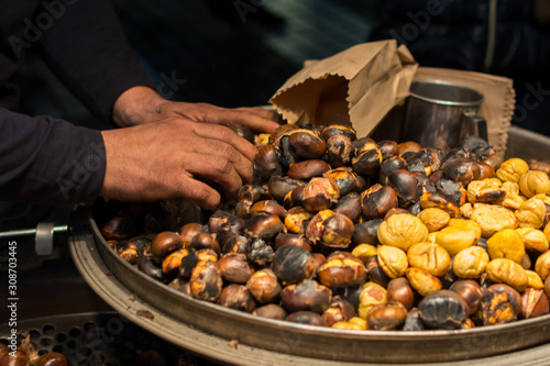 Close up of hands of chestnut vendor roasting chestnuts on a street, preparing a serving in a paper bag photo