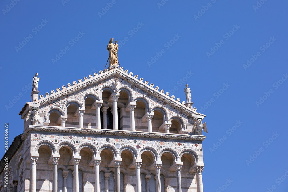 Top of facade of Pisa Cathedral with arcades and statue. Architectural details close up. Detail of the facade. Blue sky, summertime. Italy