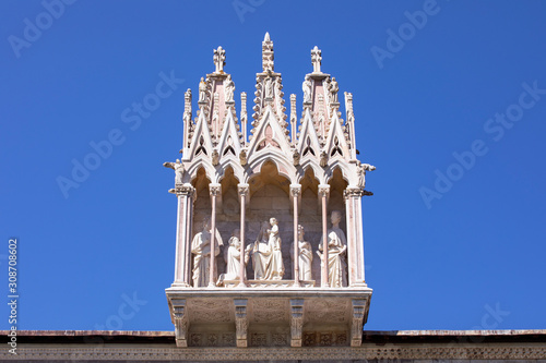 The sculpture of Holy Family over the entrance of the ancient Monumental Cemetery. Architectural detail above entrance to Camposanto Monumentale. Piazza dei Miracoli, Pisa, Tuscany, Italy. Blue sky. 