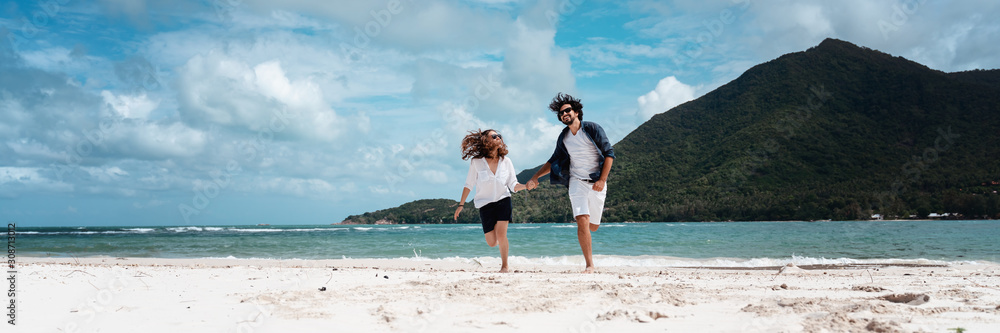 Beautiful young couple joyfully spins running on a tropical beach, Happy summer sea vacation  lifestyle design. Banner format