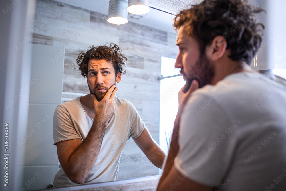 Morning hygiene, Handsome man in the bathroom looking in mirror. Reflection of handsome man with ...