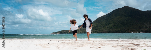 Beautiful young couple joyfully spins running on a tropical beach, Happy summer sea vacation lifestyle design. Banner format