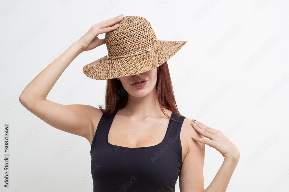 Red-haired girl in a black t-shirt and straw hat posing on a white background Red-haired girl in a black t-shirt and straw hat posing on a white background