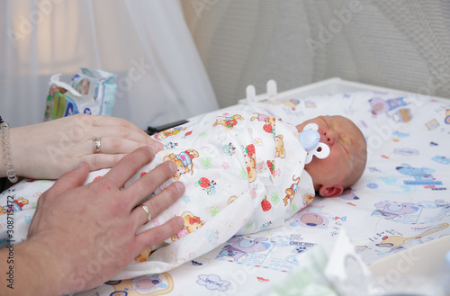 hands of mother and father or parents hug a newborn baby who is lying in bed or on a dressing table