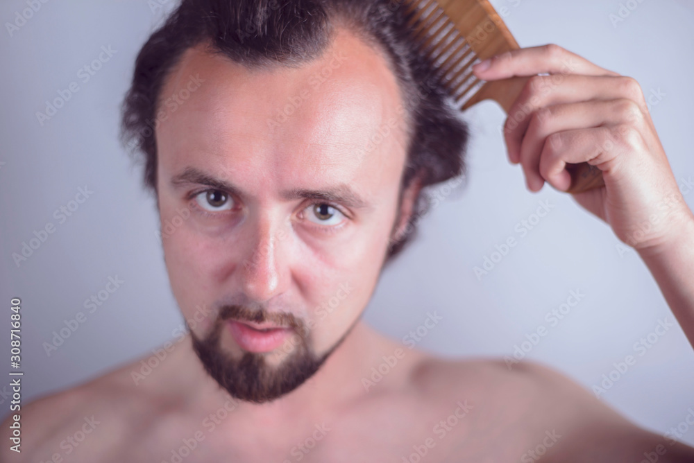 Obraz premium Portrait of a young guy with magnificent hair that falls early on his forehead. The problem of premature aging. Combing hair and indignantly looking in the mirror