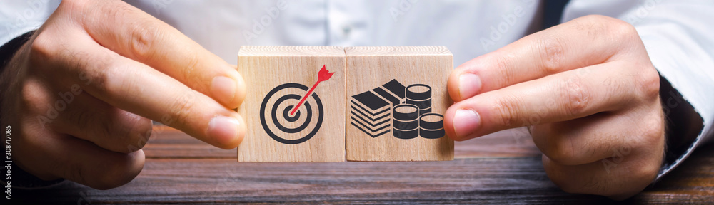 Businessman collects wooden blocks with the image of the goal and money. The concept of doing business and finance. Setting goals and objectives for maximum profit. Strategy and Planning - obrazy, fototapety, plakaty 