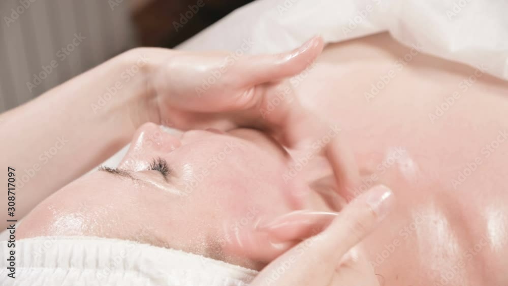 Close-up Spa facial Massage. Girl professional massage therapist does a relaxing facial massage to an attractive client of a spa salon Close-up Spa facial Massage. Girl professional massage therapist does a relaxing facial massage to an attractive client of a spa salon