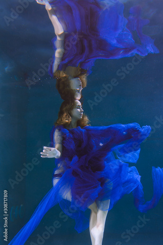 Beautiful girl in a blue dress swims underwater in the pool or in the sea.