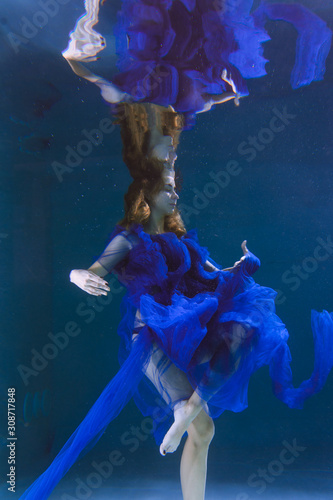 Beautiful girl in a blue dress swims underwater in the pool or in the sea.