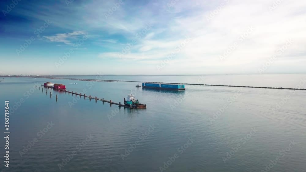 Aerial dolly shot over the mouth of Fraser river with a parked tugboat. Another tugboat towing cargo barge passing by up the river. Dramatic scenery blue sky and stratus clouds