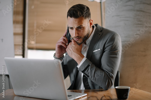 Handsome businessman in office talking on phone. Successful man in suit discussing business on phone call. 