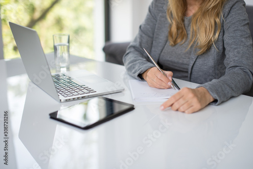 A blonde hair businesswoman working in her workstation. Businesswoman working at the desk at workplace. Woman working in home office. Woman sitting at desk and working with laptop and glass of water.
