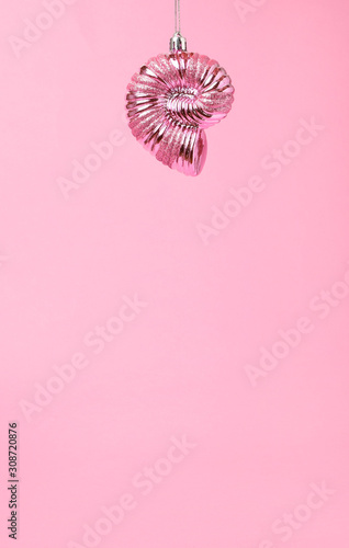 Christmas toy in the form of a pink shell hangs from above on a pastel pink background. The concept of the new year and relaxation. Vertical photo  copy space