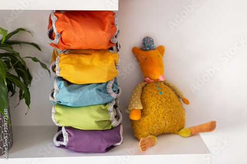 five colored washable diapers stacked on a shelf with a plush, horizontal