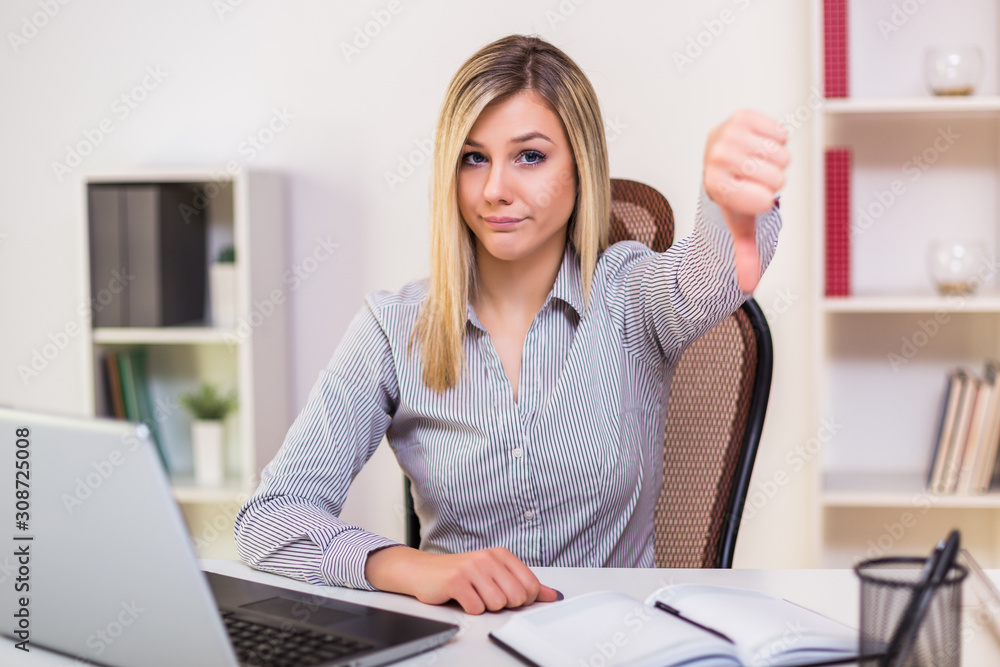 Businesswoman showing thumb down while working in her office. Businesswoman showing thumb down while working in her office.