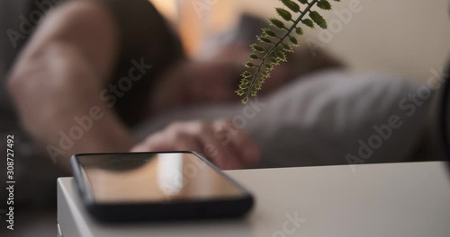 Blurred view of man waking up and using mobile phone in bed