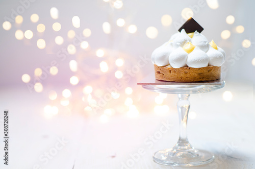 Gorgeous lemon meringue tart on glass stand, Christmas lights in background 