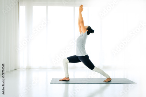 Side view portrait of beautiful young woman doing yoga or pilates exercise. Standing in Warrior one pose, Virabhadrasana, working out,In the white room indoor full length © Nipapun