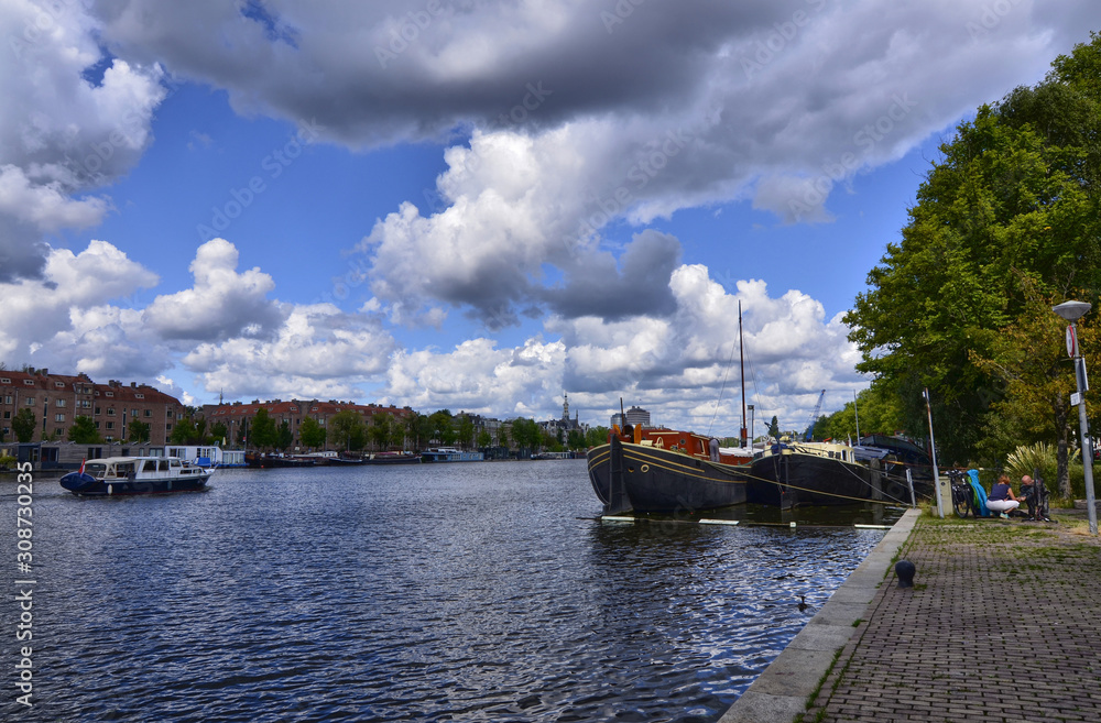 Amsterdam, Holland, August 2019. View of the Amstel River, outskirts of the city. A large moored boat is used as a houseboat. Sunny day with blue sky and white clouds.