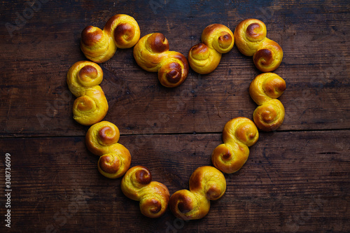 Swedish traditional christmas bun Lussekatter or Lussebullar on a rustic wooden table, in the shape of a heart. photo