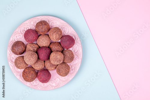 Homemade Raw Vegan Cacao Energy Balls on Vintage Plate on Trend Blue and Pink Paper Background. Healthy Chocolate Snacks from Nuts and Dates. Concept of Natural Vegetarian Handmade Dessert
