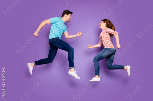 Full body photo of crazy two people guy lady jumping up high opposite looking eyes running competitions wear casual blue striped shirts jeans footwear isolated purple color background