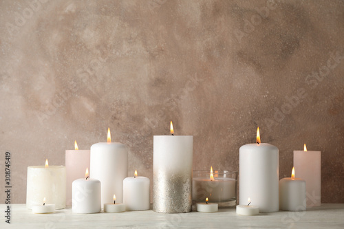 Burning candles on white wooden table against brown background, space for text